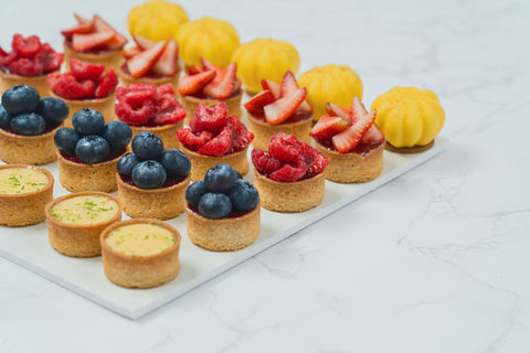 Side Image of a 25-piece assortment of Mini Mix Tarts from Laura's Home Bakery, showcasing their vibrant fruit fillings and golden-brown, buttery crusts.