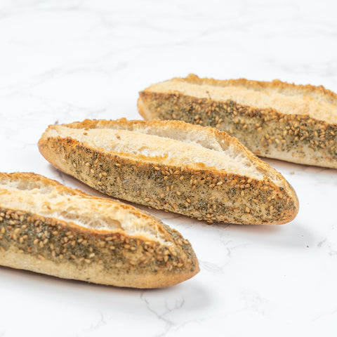Closeup Image of a Mini Zaatar Sourdough Baguette from Laura's Home Bakery, showcasing its rustic exterior and the fragrant blend of za'atar herbs mixed into the dough.