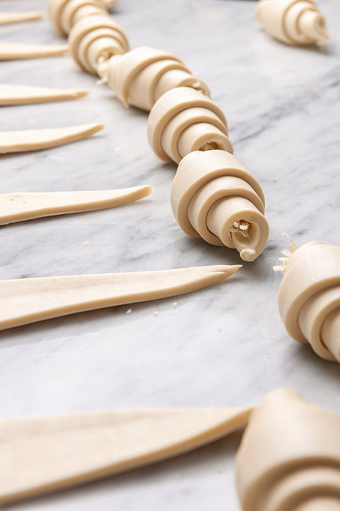 Croissants in the process of being prepared, with skilled hands expertly shaping the dough into classic triangular forms.