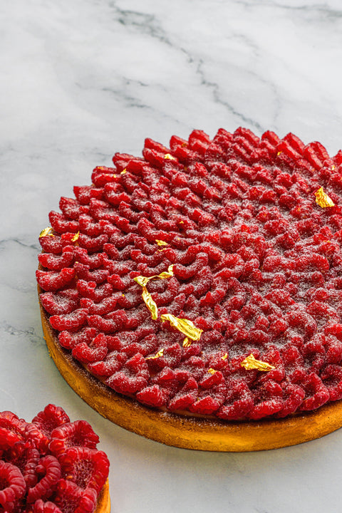 Delectable Raspberry Tart, adorned with fresh raspberries, set on a golden crust with a delicate dusting of powdered sugar
