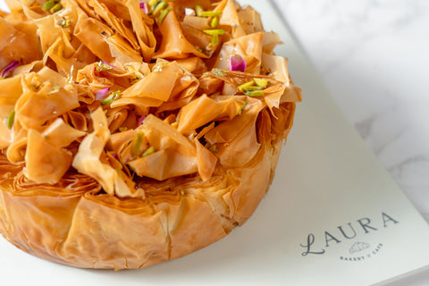 A baklava cheese cake topped with phyllo dough and nuts, served on a plate.
