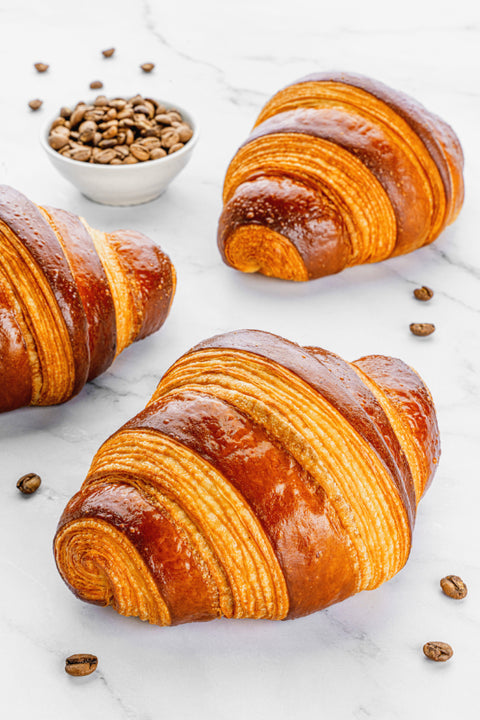 Image of a Coffee Croissant from Laura's Home Bakery, a delectable treat designed to complement the rich flavors of coffee, showcasing its golden-brown, flaky exterior beside coffee beans