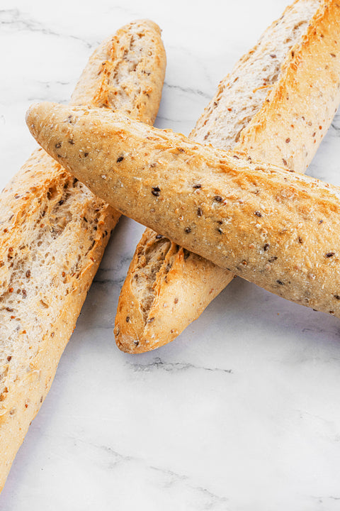 Image of a Multigrain Sourdough Baguette from Laura's Home Bakery, showcasing its rustic crust, chewy interior, and a medley of nourishing grains