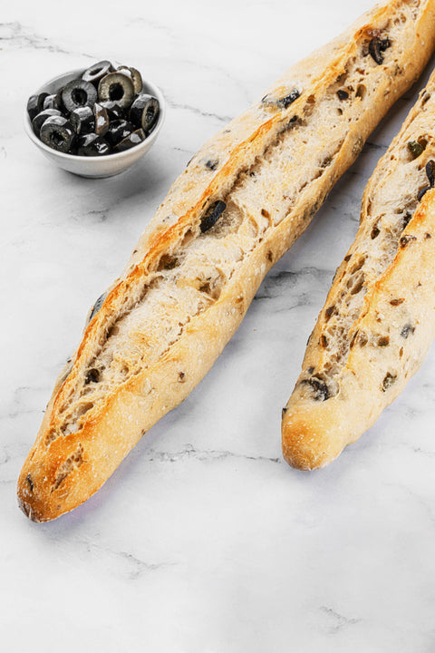 Image of an Olive Sourdough Baguette from Laura's Home Bakery, showcasing its crusty exterior, chewy interior, and a generous scattering of briny olives.