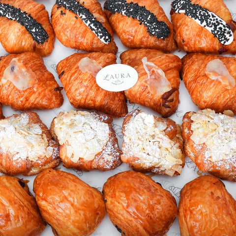A variety of croissants with different fillings, including almond and chocolate, displayed on a surface with the brand name 'Laura' visible on a tag.