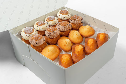 An open pastry box containing a variety of baked goods, including choux vanilla salted caramel and hazelnut Choco madeleine.