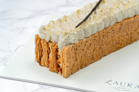 Close up Image of a Vanilla Mille Feuille from Laura's Home Bakery, showcasing its delicate layers of flaky puff pastry and velvety vanilla custard, finished with a dusting of powdered sugar.