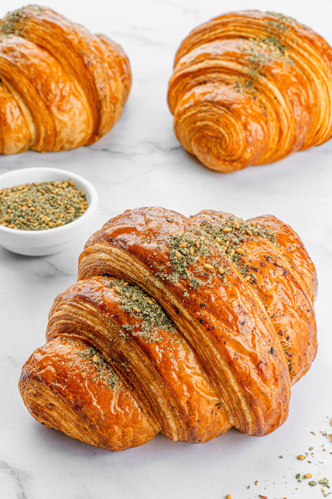 Image of a Zaatar Croissant from Laura's Home Bakery, showcasing its flaky texture and generous seasoning of aromatic Zaatar herbs.