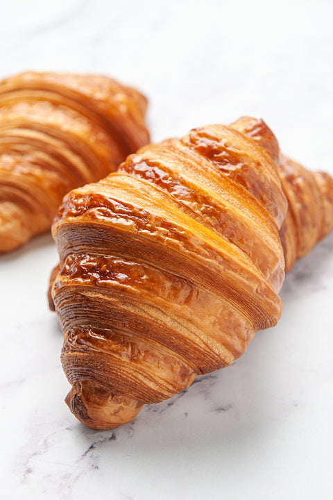 Close-up image of a single, perfectly baked Plain Pure Butter Croissant from Laura's Home Bakery, showcasing its golden, flaky layers and irresistible buttery aroma.