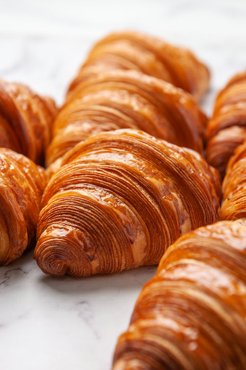 An arrangement of freshly baked Plain Pure Butter Croissants from Laura's Home Bakery, creating a delightful display of golden, flaky pastries with an inviting buttery aroma.