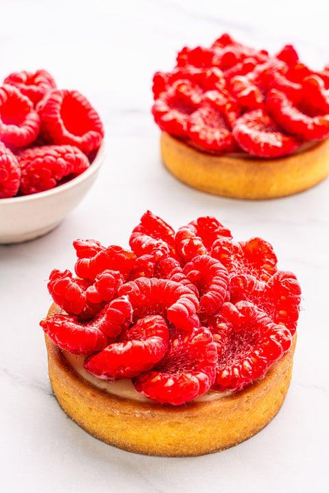 Close-up view of a mini Raspberry Tart from Laura's Home Bakery, highlighting the meticulous arrangement of plump raspberries on a petite, golden pastry crust.